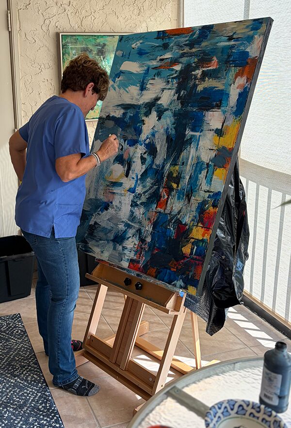 Janice Savage painting a large blue abstract acrylic canvas in her South Florida art studio.